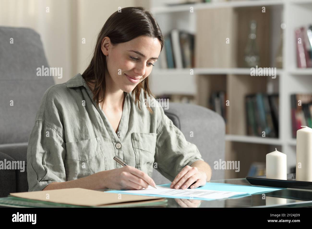 Glückliche Frau, die zu Hause Papierdokumente liest und unterschreibt Stockfoto