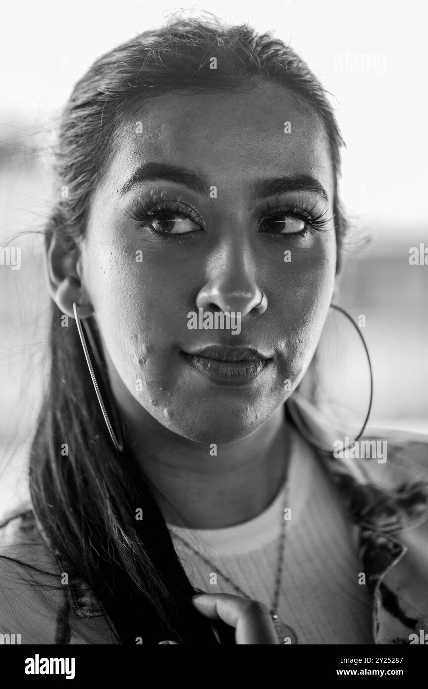 Indische Frau mit stilvollem Denim-Outfit und auffälligem Make-up, die in der Nähe eines Bahnhofs läuft und ihr Telefon benutzt und urbanen Lifestyle und Mode repräsentiert. Stockfoto