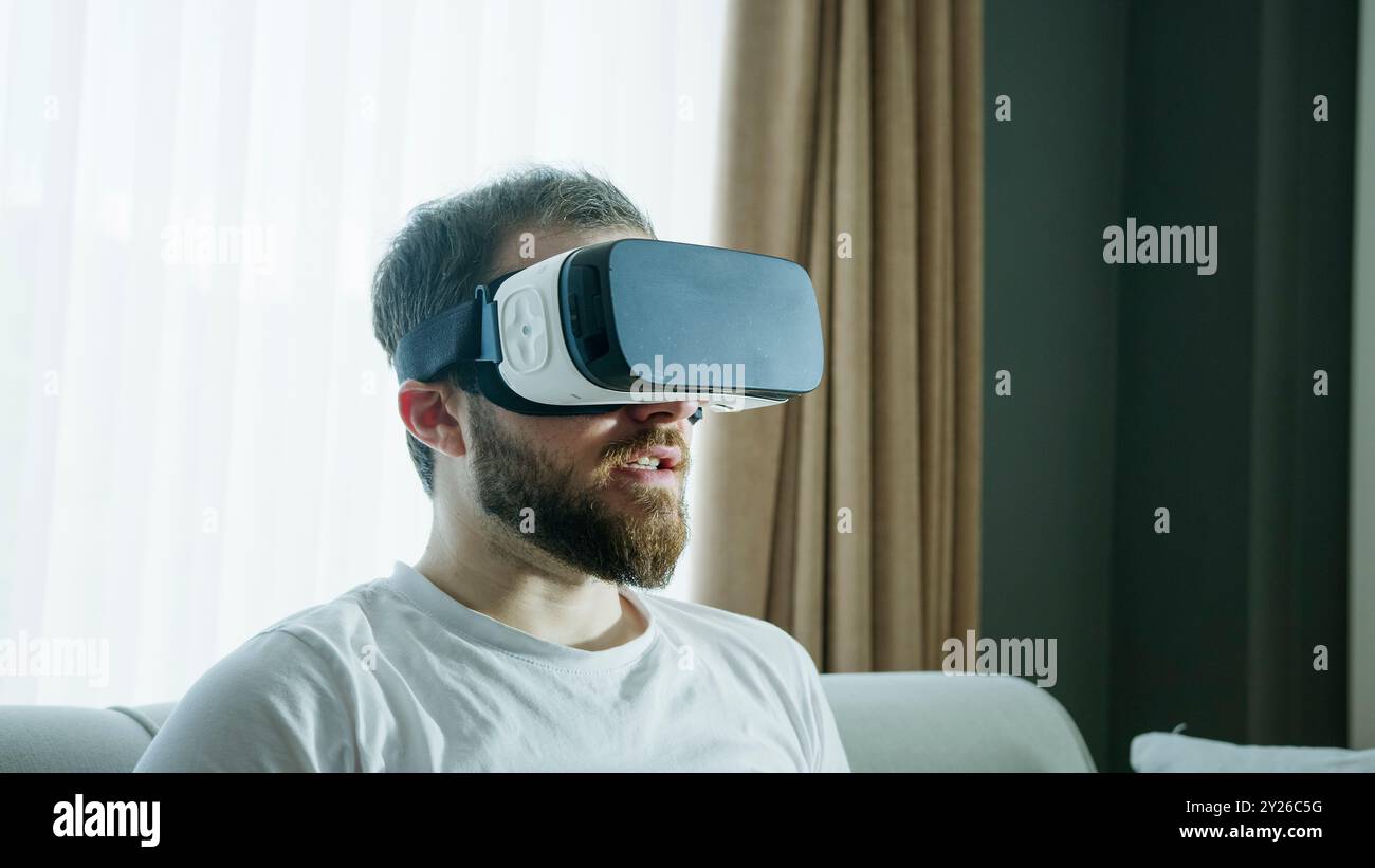 Ein Mann erkundet die virtuelle Realität mit einem VR-Headset, das vollständig in ein digitales Erlebnis eingetaucht ist. Die Interaktion mit der virtuellen Umgebung, der fortschrittlichen Technologie Stockfoto