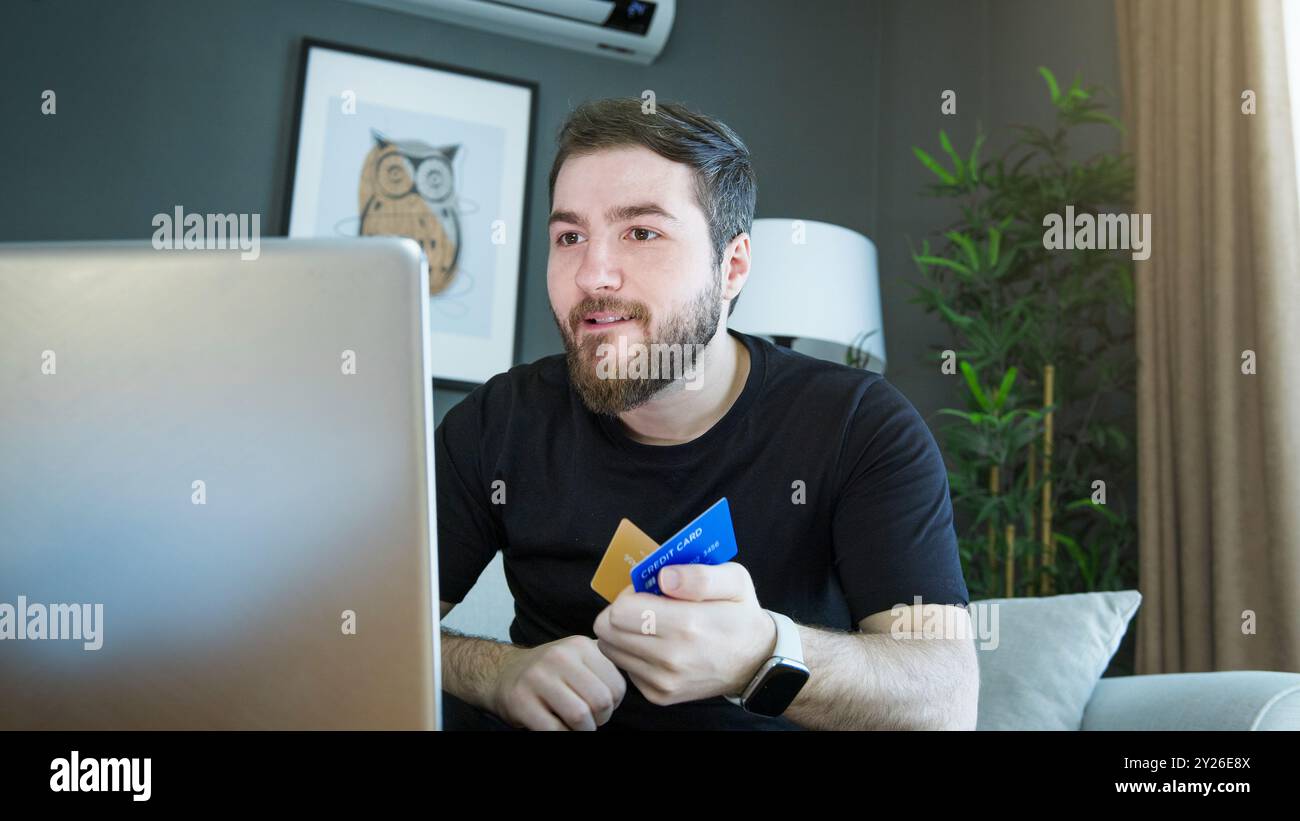 Ein Mann sitzt auf der Couch und kauft online mit den Kreditkarten auf dem Laptop. Stockfoto