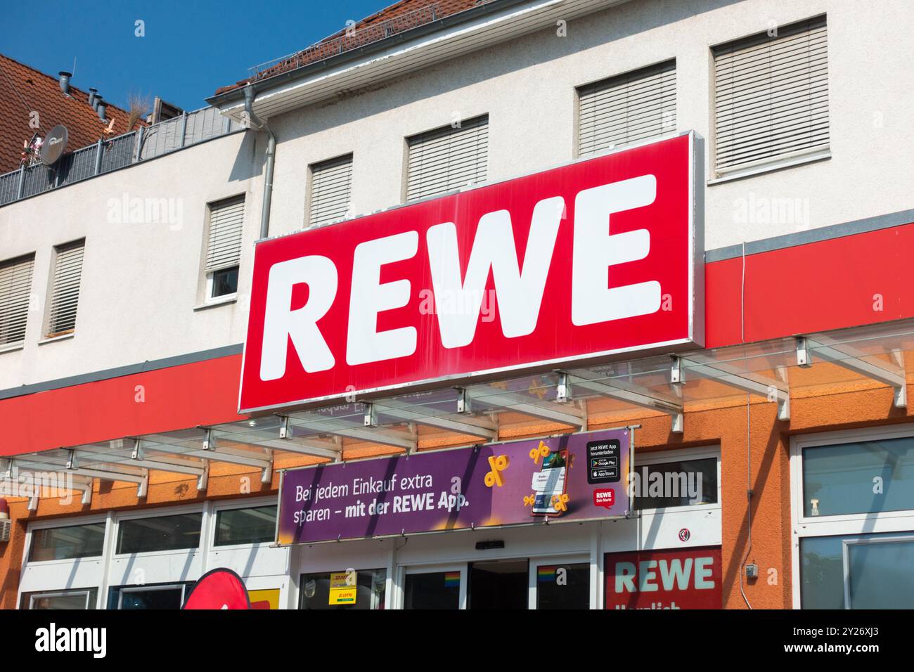 Schild mit dem REWE-Logo über dem Eingang zum Supermarkt Deutschland Europa Außenansicht eines REWE-Supermarktes mit Schildern und Werbebanner Stockfoto