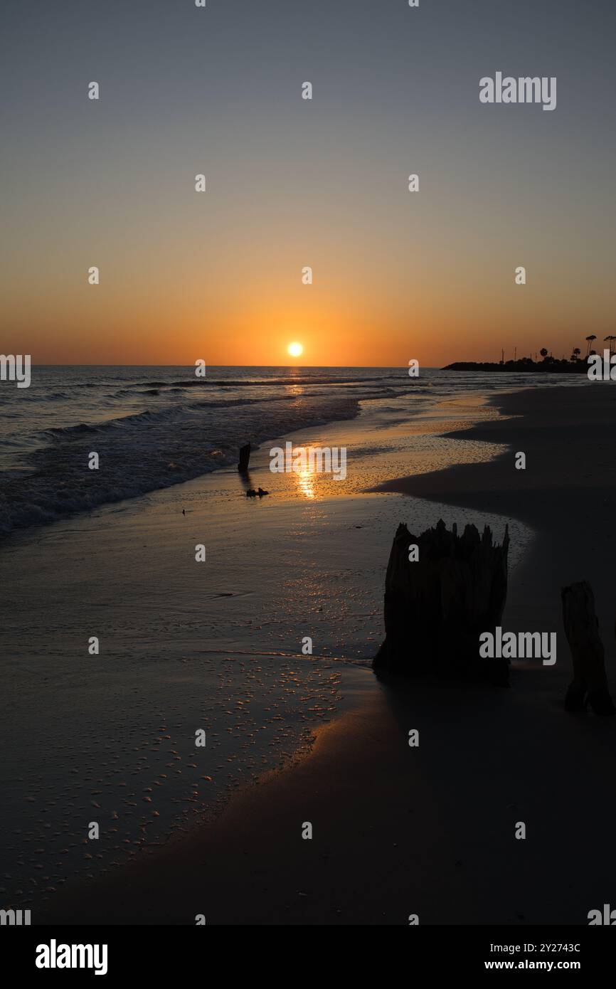 Wunderschöner Sonnenuntergang entlang des Strandes, während Wellen über warmen, reflektierenden Sand ein- und ausrollen. Ruhige und malerische Aussicht auf das Urlaubsziel Stockfoto