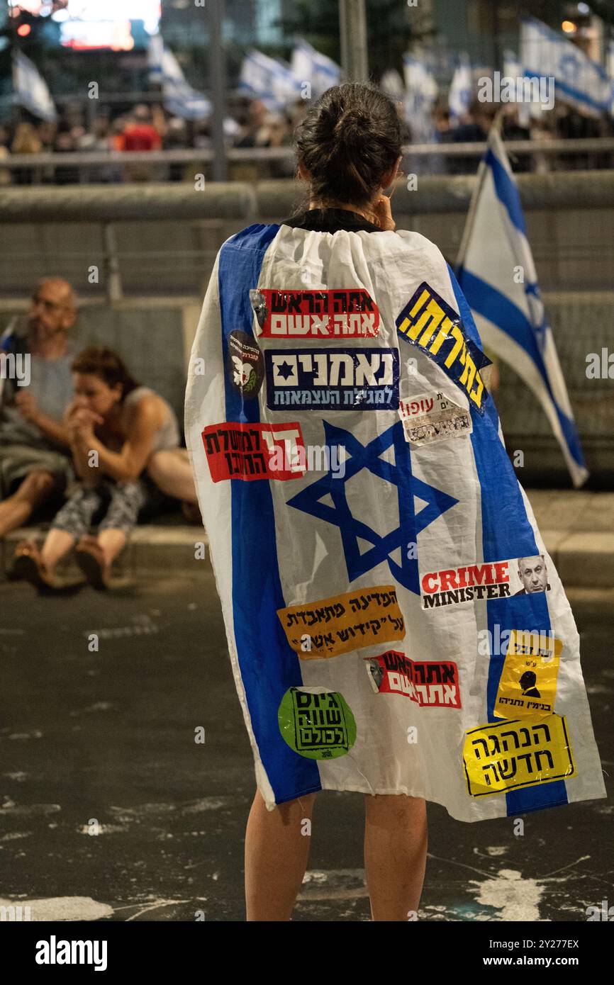 Ein Demonstrant trägt eine israelische Flagge mit hebräischen Protestaufklebern während der Anti-Regierungs-Kundgebung am 7. September 2024 in Tel Aviv für einen Geiselvertrag Stockfoto Ein Demonstrant trägt eine israelische Flagge mit hebräischen Protestaufklebern während der Anti-Regierungs-Kundgebung am 7. September 2024 in Tel Aviv für einen Geiselvertrag Stockfoto