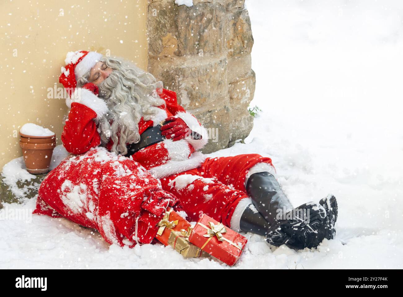 Der Weihnachtsmann schläft im Schnee und lehnt sich an das Haus Stockfoto