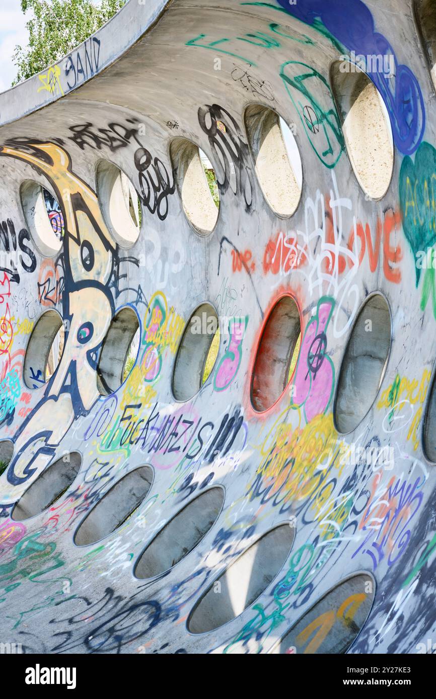 Betonwand mit kreisrunden Löchern und Grafitti im Sonnenschein Stockfoto