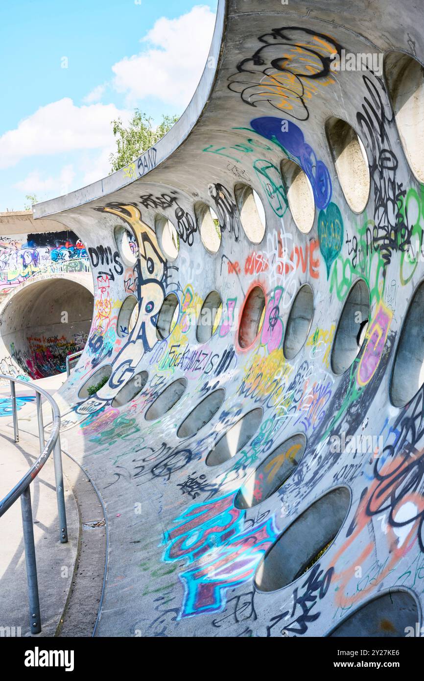 Betonwand mit kreisrunden Löchern und Grafitti im Sonnenschein Stockfoto