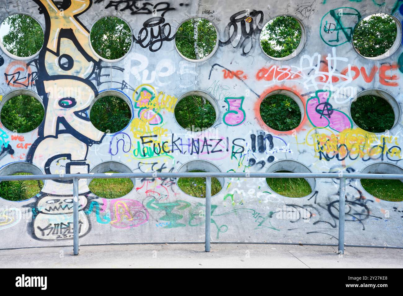 Betonwand mit kreisrunden Löchern und Grafitti im Sonnenschein Stockfoto