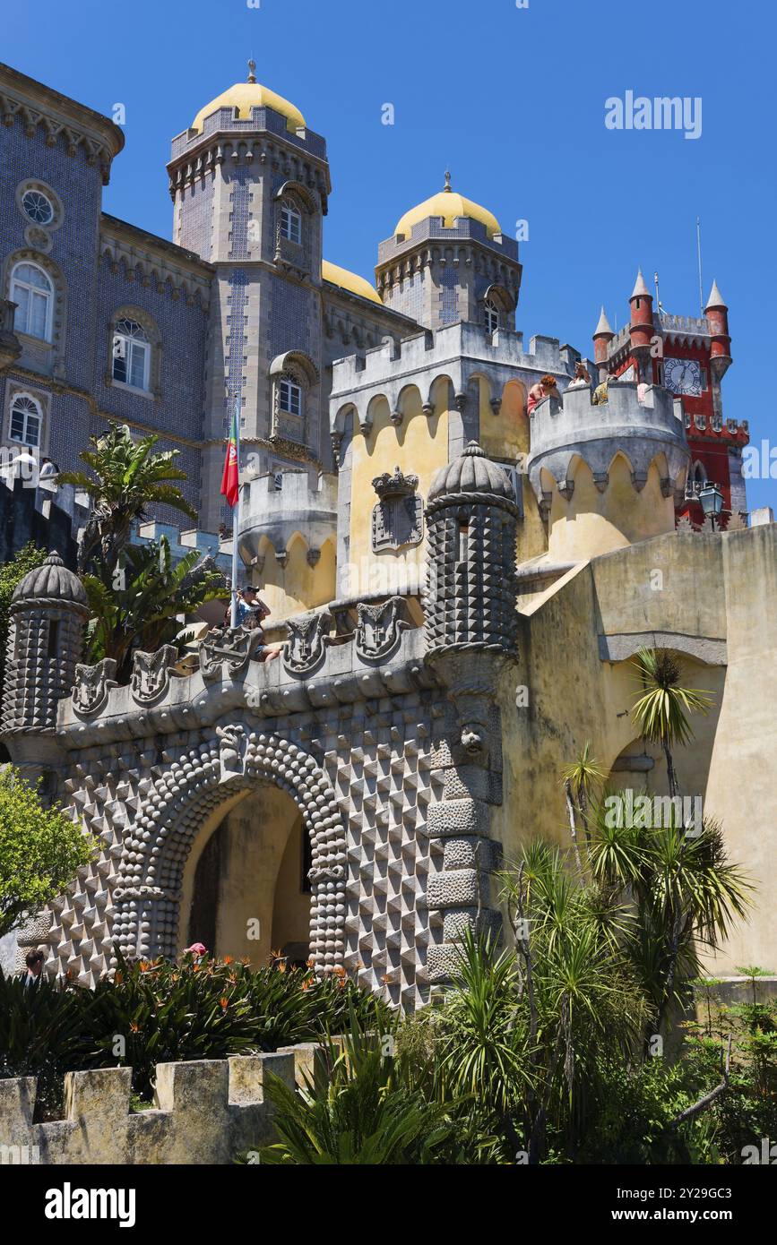 Historisches Schloss mit Türmen, Steinbauten und Pflanzen im Vordergrund unter blauem Himmel, Palacio Nacional da Pena, Pena National Palace, Sintra, L Stockfoto