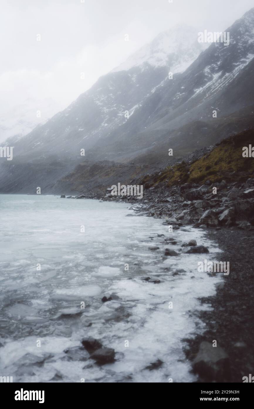 Blick auf einen gefrorenen See vor schneebedeckten Bergen mit nebeligem Himmel und felsiger Küste, Hooker Valley Track, Neuseeland, Ozeanien Stockfoto