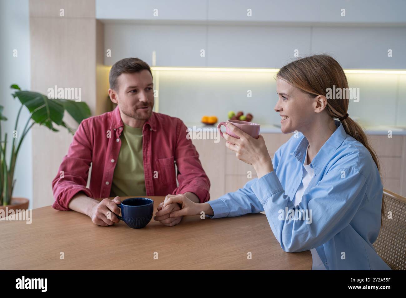 Lächelndes junges Paar, das in die Ferne starrt, während es zusammen Tee und Frühstück in der Küche hatte Stockfoto