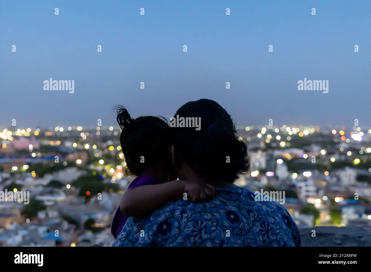 Hintergrundbeleuchtete Aufnahme von Mutter und Sohn, die den Sonnenuntergang am Horizont der Stadt in der Abenddämmerung beobachten Stockfoto