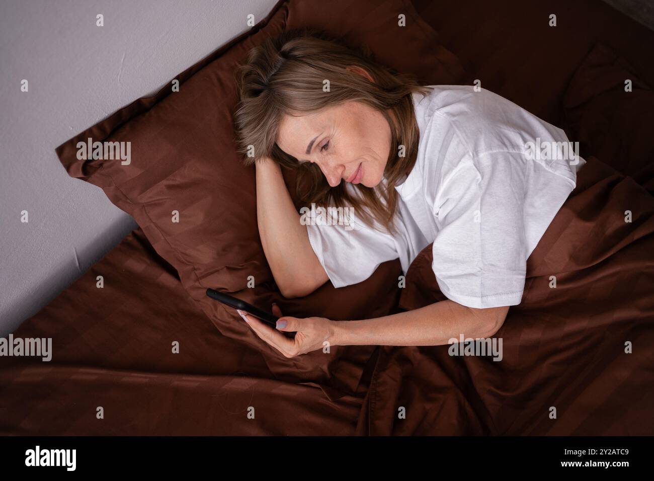 Depression der reiferen Frau am Telefon, das sich auf dem Bett entspannt. Müde, psychische Gesundheit und einsame Dame, die in den sozialen Medien in ihrem Schlafzimmer zu Hause surft, Top Stockfoto