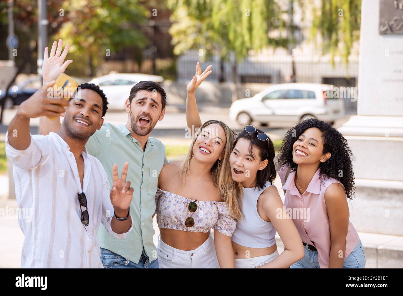 Fünf Freunde lächeln, winken und machen an einem sonnigen Tag ein lebhaftes Selfie im Freien, um einen lustigen Moment zusammen mit fröhlichen Ausdrücken und einer entspannten Atmosphäre festzuhalten. Stockfoto