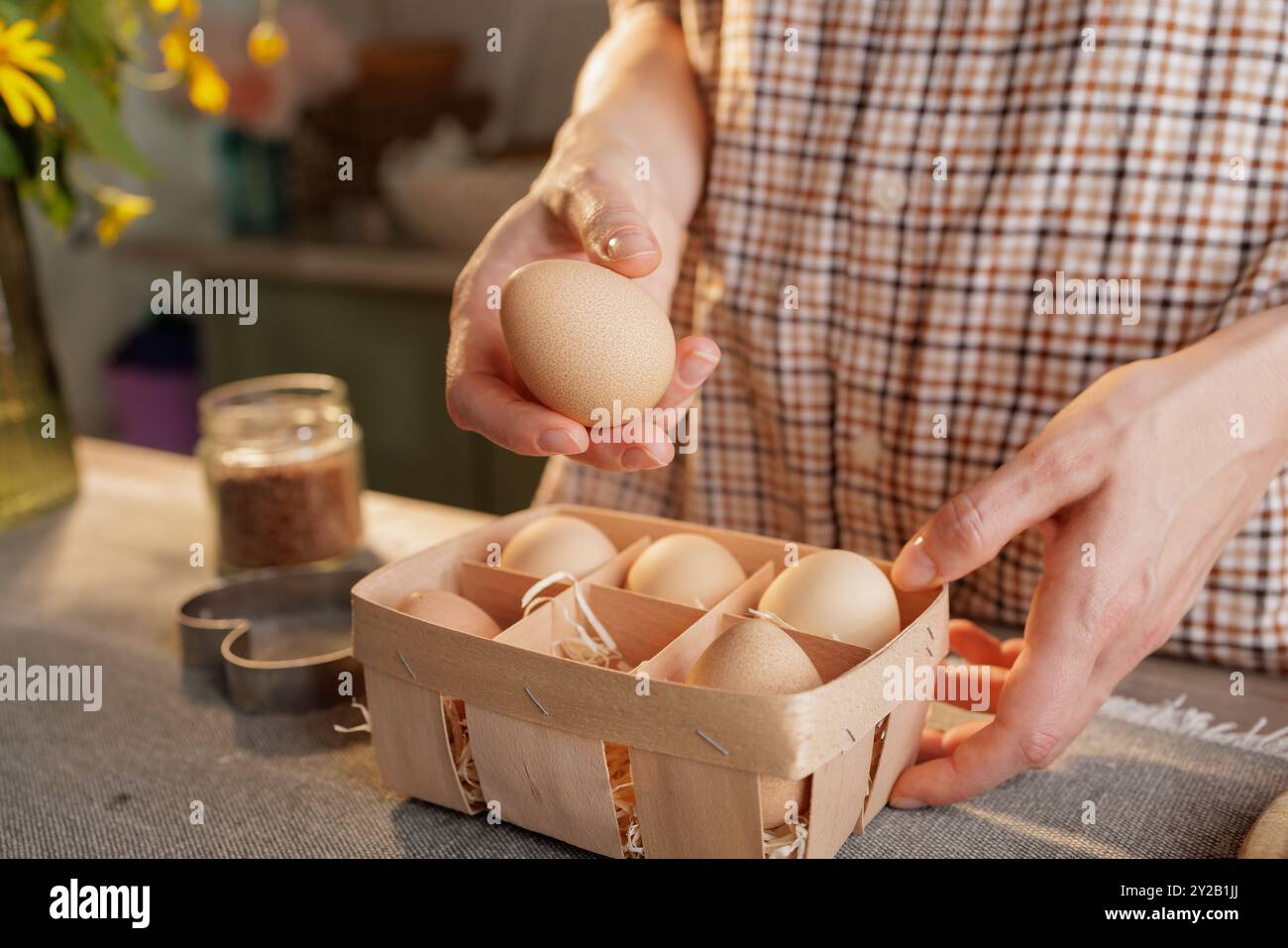 Nahaufnahme der Hand der Frau, die Ei über Korb mit mehreren Eiern hält, Küchenhintergrund. Konzept für frische Bio-Eier Stockfoto