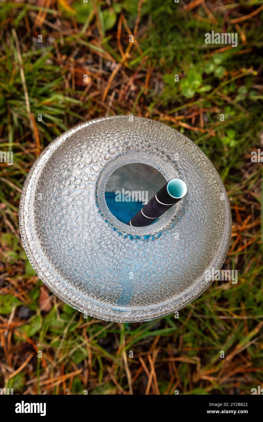 Klarer Trinkbecher aus Kunststoff mit blauem Limonade auf dem Boden im Freien Stockfoto