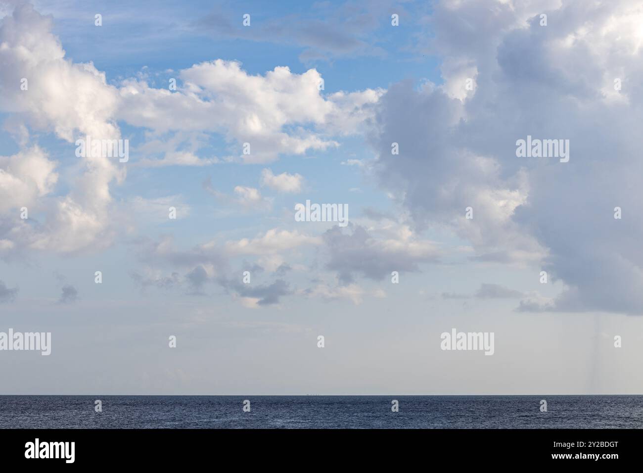 Dunklere dramatische Wolken und Sonnenstrahlen am blauen Himmel, von der Küste aus aufgenommen Stockfoto