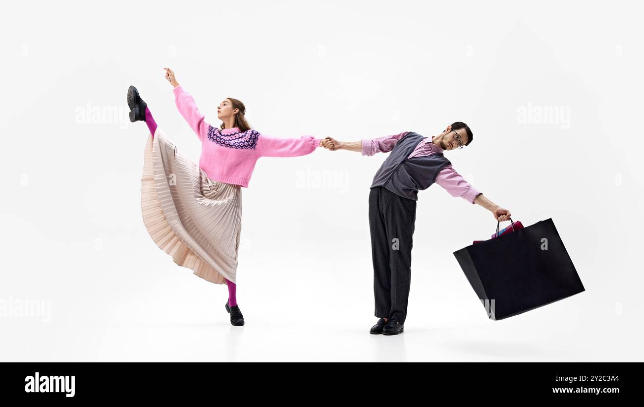 Die Frau tritt hoch, während sie die Hand ihres Partners hält. Beide tragen Einkaufstaschen vor weißem Studiohintergrund. Stockfoto