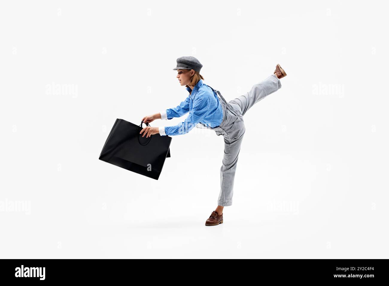 Eine Frau kleidete Vintage-Kleidung mit Einkaufstaschen, die Stil und Bewegung anmutig vor weißem Studiohintergrund ausbalancierte. Stockfoto