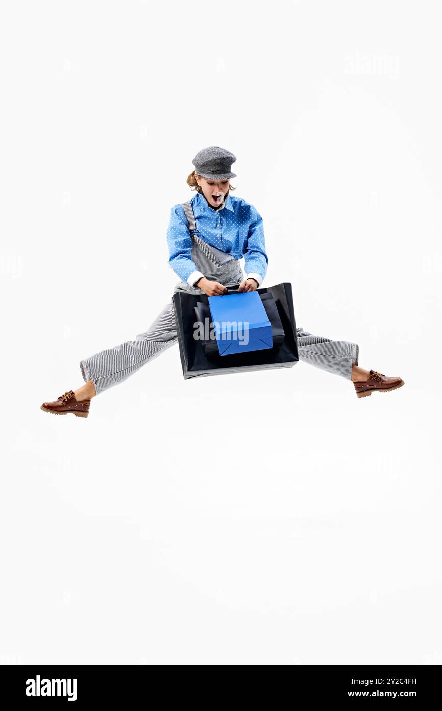 Vor Freude springen, lächelnde junge Frau mit Einkaufstaschen in der Hand vor weißem Studiohintergrund mit negativem Raum. Stockfoto