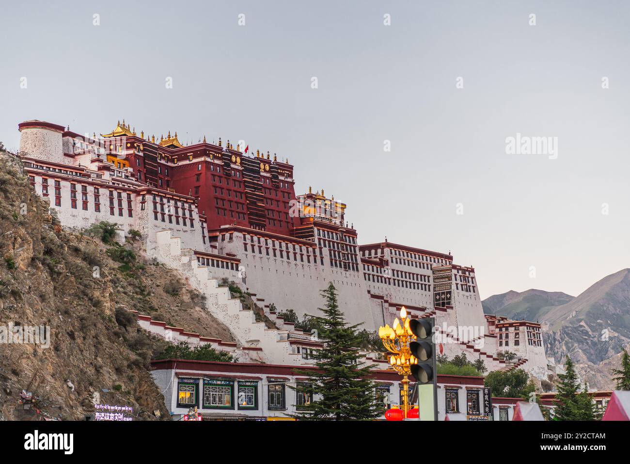 Die abgewinkelte Front des Potala-Palastes wurde oben und die Straßenlandschaft unten unter einem klaren blauen Himmel während des frühen Abends in Lhasa, Tibet, angehoben. Horizontal Stockfoto