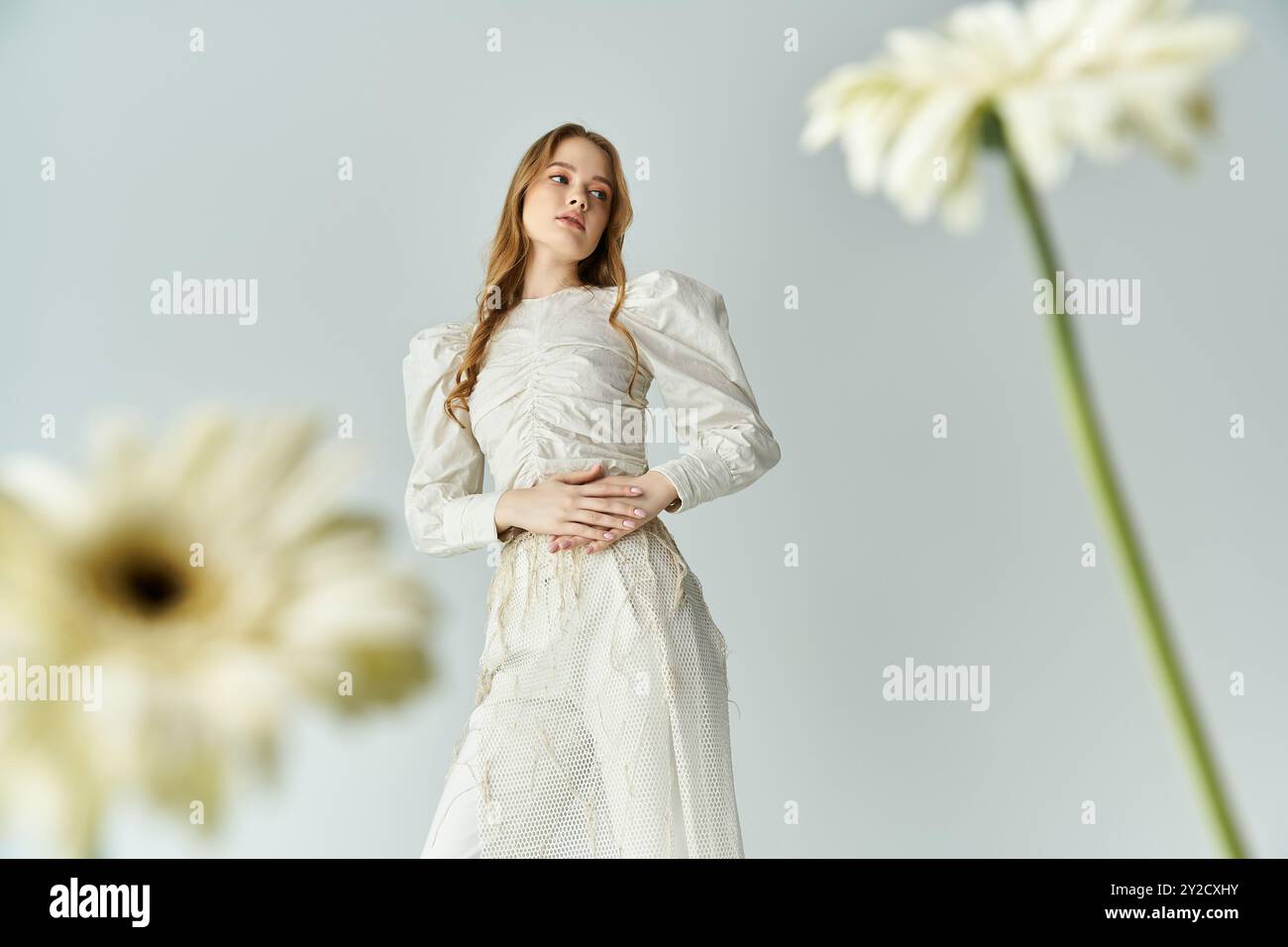 Eine junge Frau posiert anmutig mit Blumen in einer ruhigen, künstlerischen Umgebung. Stockfoto