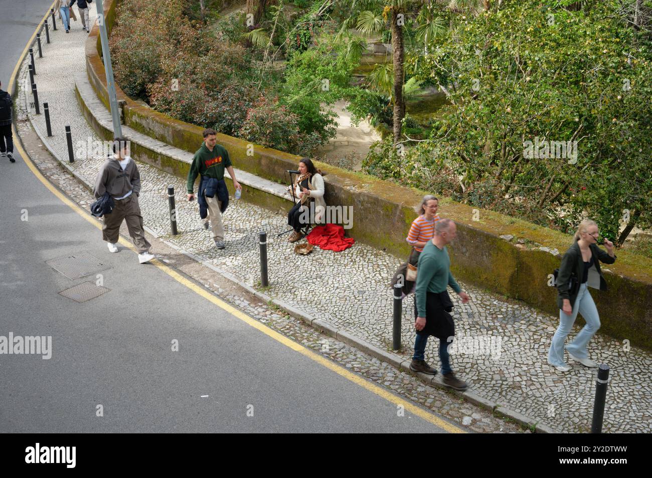 Eine Straßenmusikerin spielt ihr harfenähnliches Instrument auf einem Kopfsteinpflasterweg in Sintra, Portugal, während die Menschen vorbeigehen Stockfoto