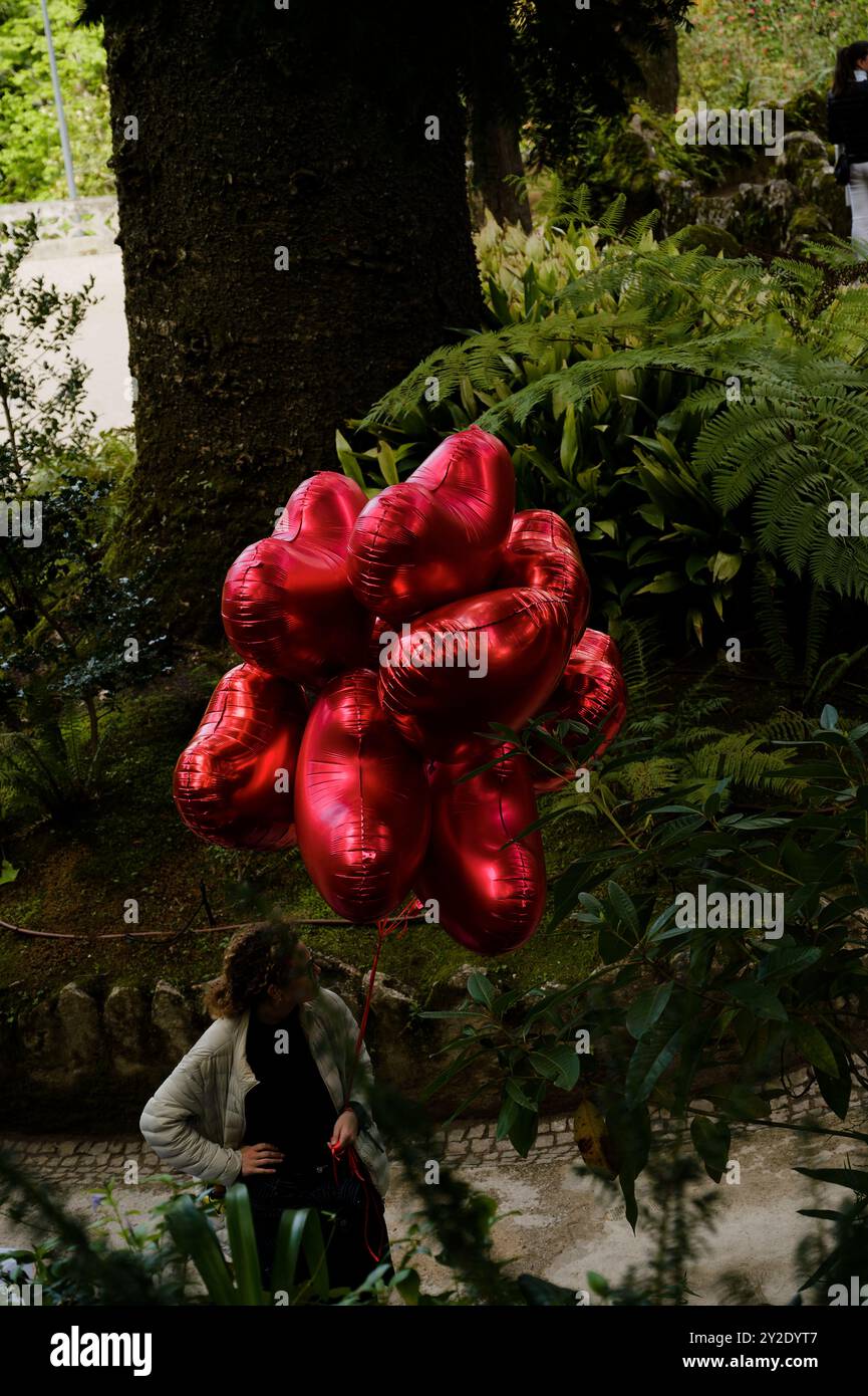 In Quinta da Regaleira schweben leuchtend rote Ballons in Herzform vor einer üppigen Gartenkulisse Stockfoto