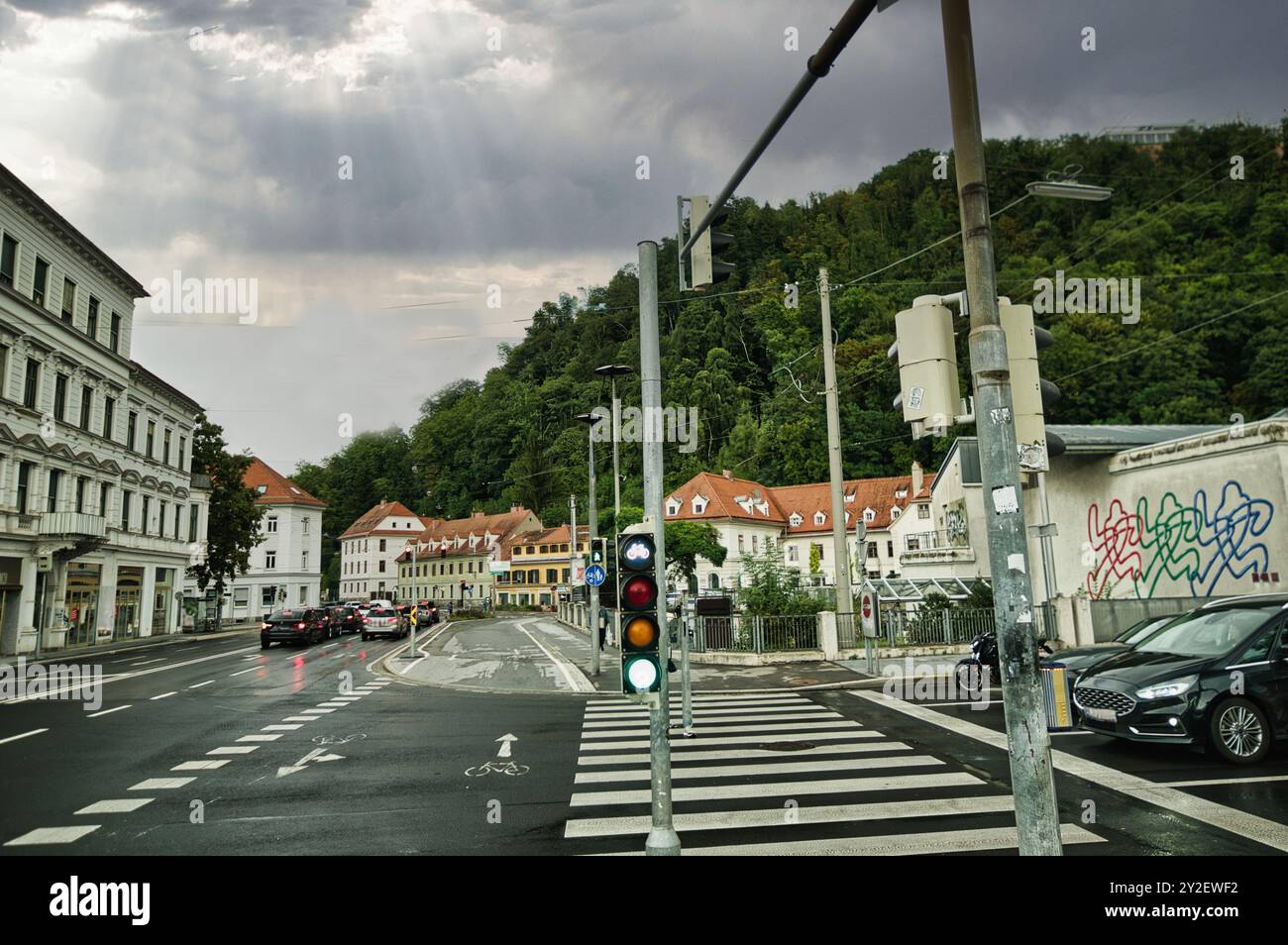 Stadt Graz in Österreich mit Straßen, Autos, Gebäuden, Motorrädern, Ampeln, nach Sturm und vor Sturm, Sturmwolken, Hügel, Wald, Bäume, in Stockfoto