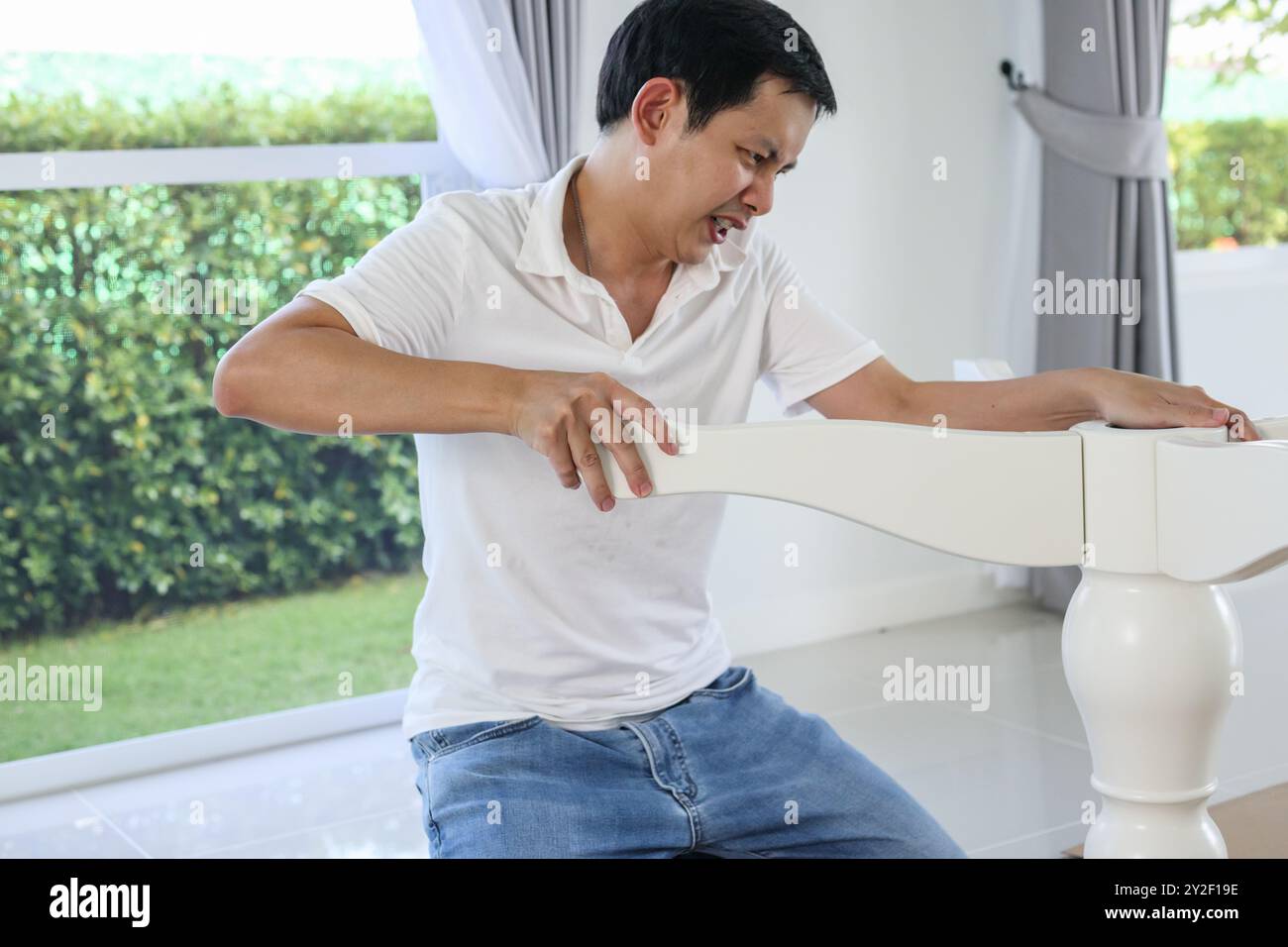 Asiatischer Mann, der weiße Tischmöbel zu Hause zusammenbaut Stockfoto