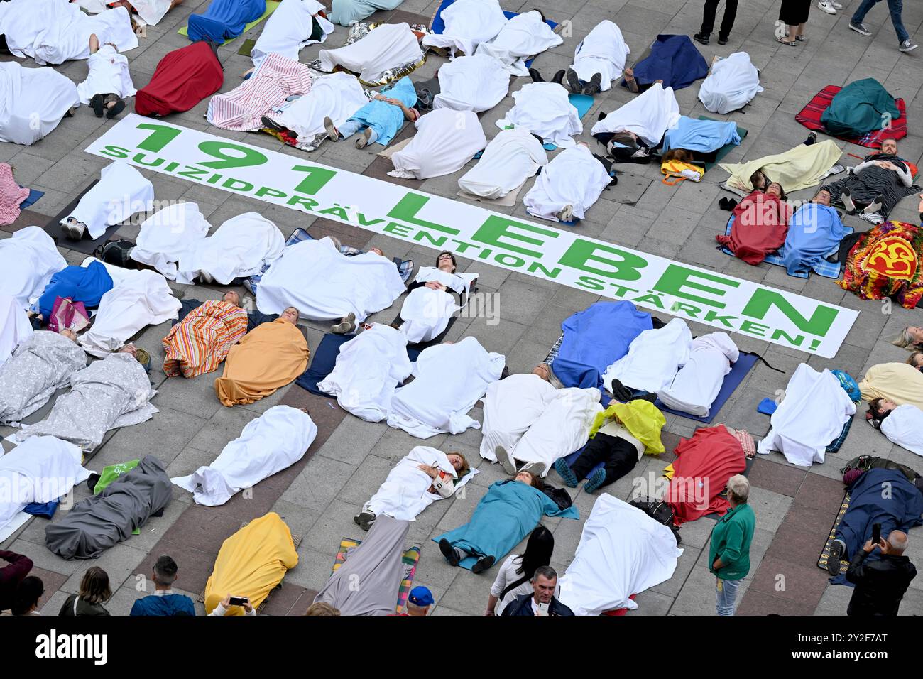 München, Deutschland. September 2024. Anlässlich des Welttages zur Suizidprävention liegen Teilnehmer einer Allianz von Krisen- und Beratungsdiensten auf dem Münchner Marienplatz in Blätter gewickelt, die die 191 Menschen repräsentieren, die 2022 in München durch Selbstmord starben. 2023 stieg diese Zahl auf 207 an. Quelle: Felix Hörhager/dpa/Alamy Live News Stockfoto