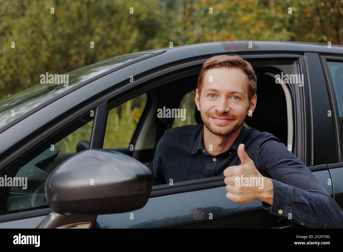 Ein glücklicher Fahrer zeigt Daumen hoch und lächelt in die Kamera im Auto. Stockfoto