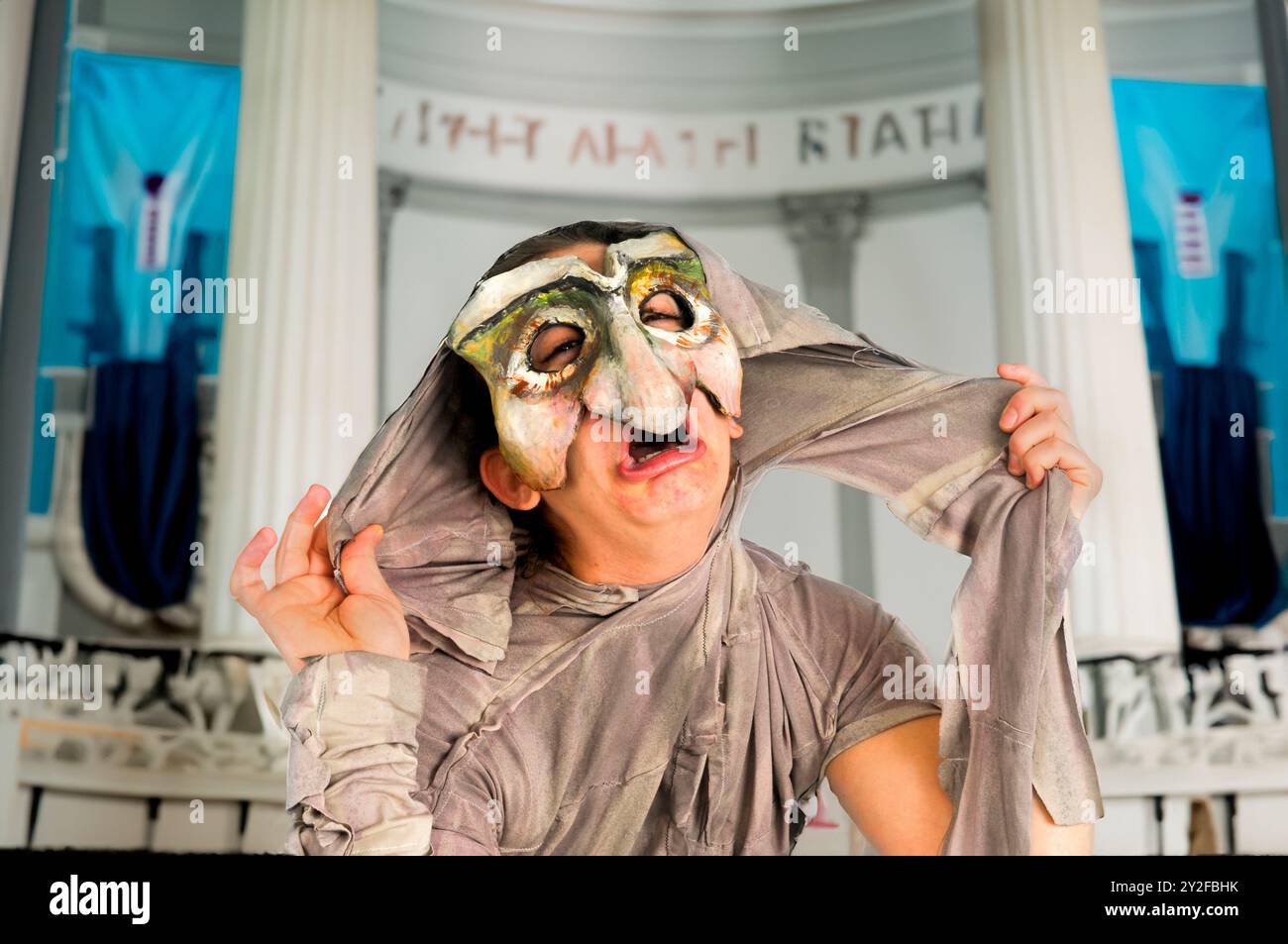 Digital verbessertes Bild eines maskierten Schauspielers in einem physischen Theater mit einem antiken griechischen Bühnenhintergrund Stockfoto