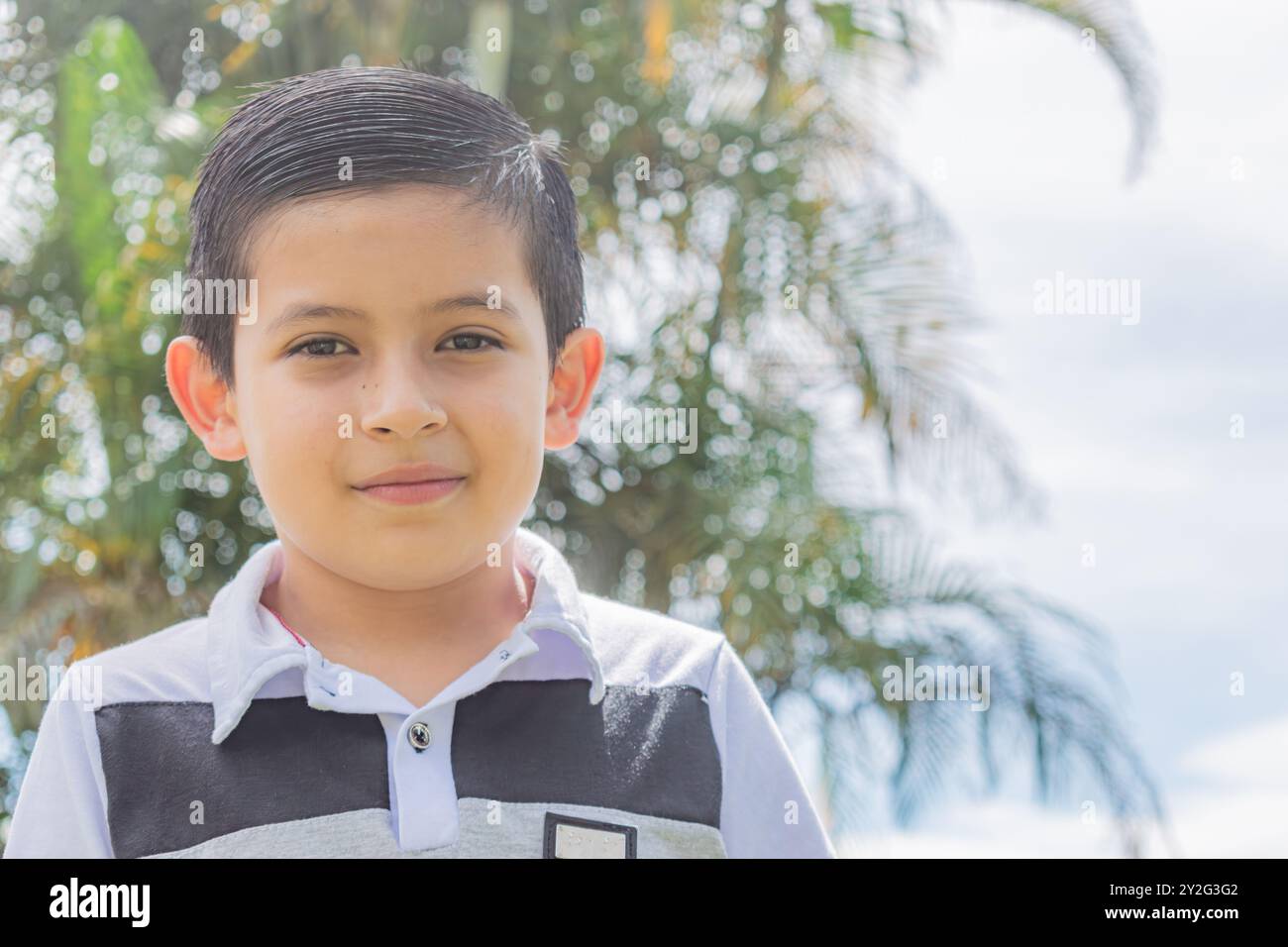 Nahaufnahme des Gesichts eines Latino-Jungen, der an einem sonnigen Tag draußen auf einem Palmenfeld in die Kamera schaut Stockfoto