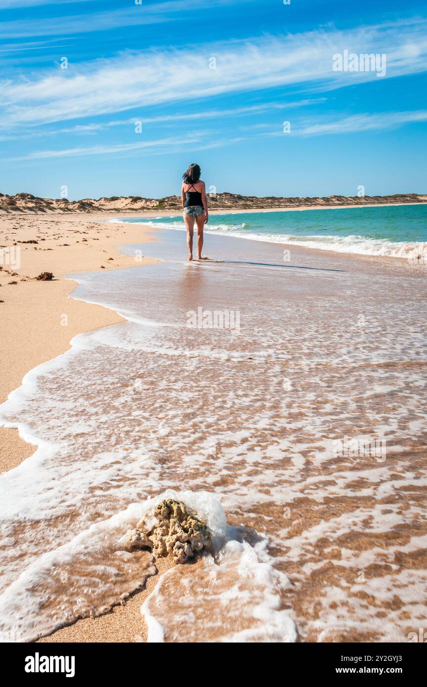 Tote Korallen im Vordergrund, schäumende Küsten, während ein Strandgänger an einem unberührten Strand auf der beliebten Halbinsel Exmouth in Western Australia spaziert. Stockfoto