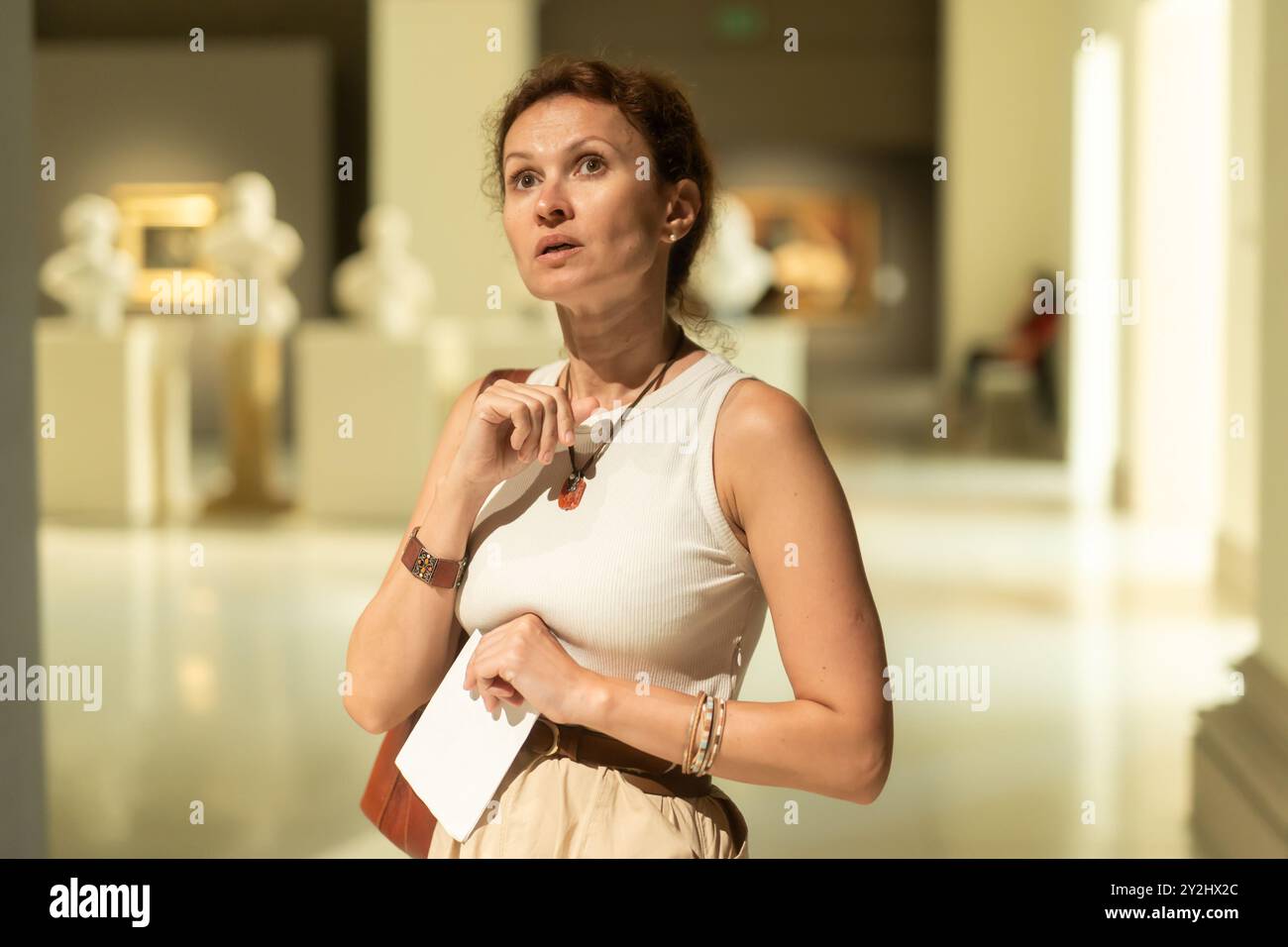 Interessierte Frau, die sich im Museum die klassischen Statuen genauer anschaut und den Tourbogen in der Hand hält Stockfoto