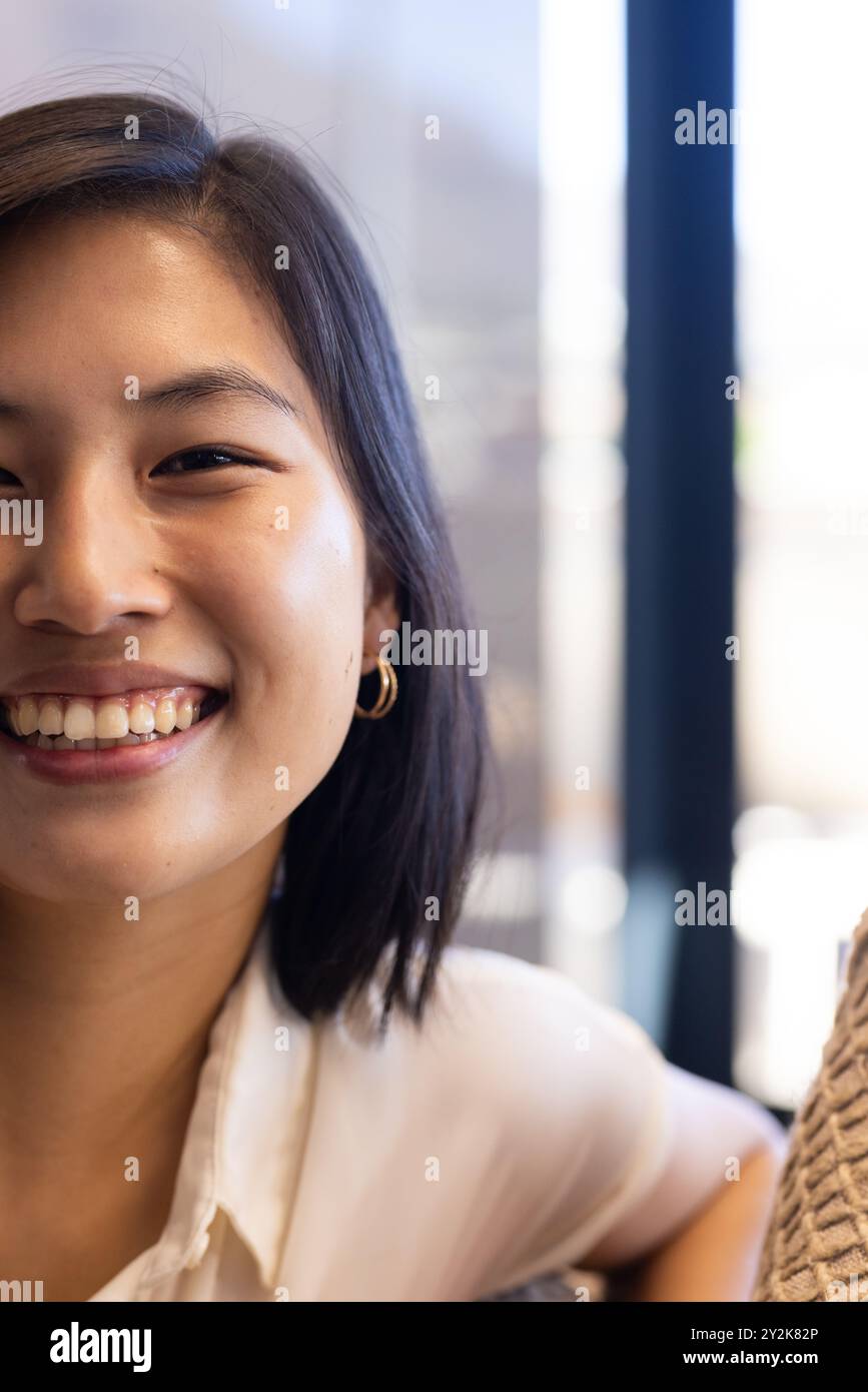 Im Büro lächelnde asiatische Frau mit kurzen Haaren, die in Innenräumen Creolen trägt Stockfoto