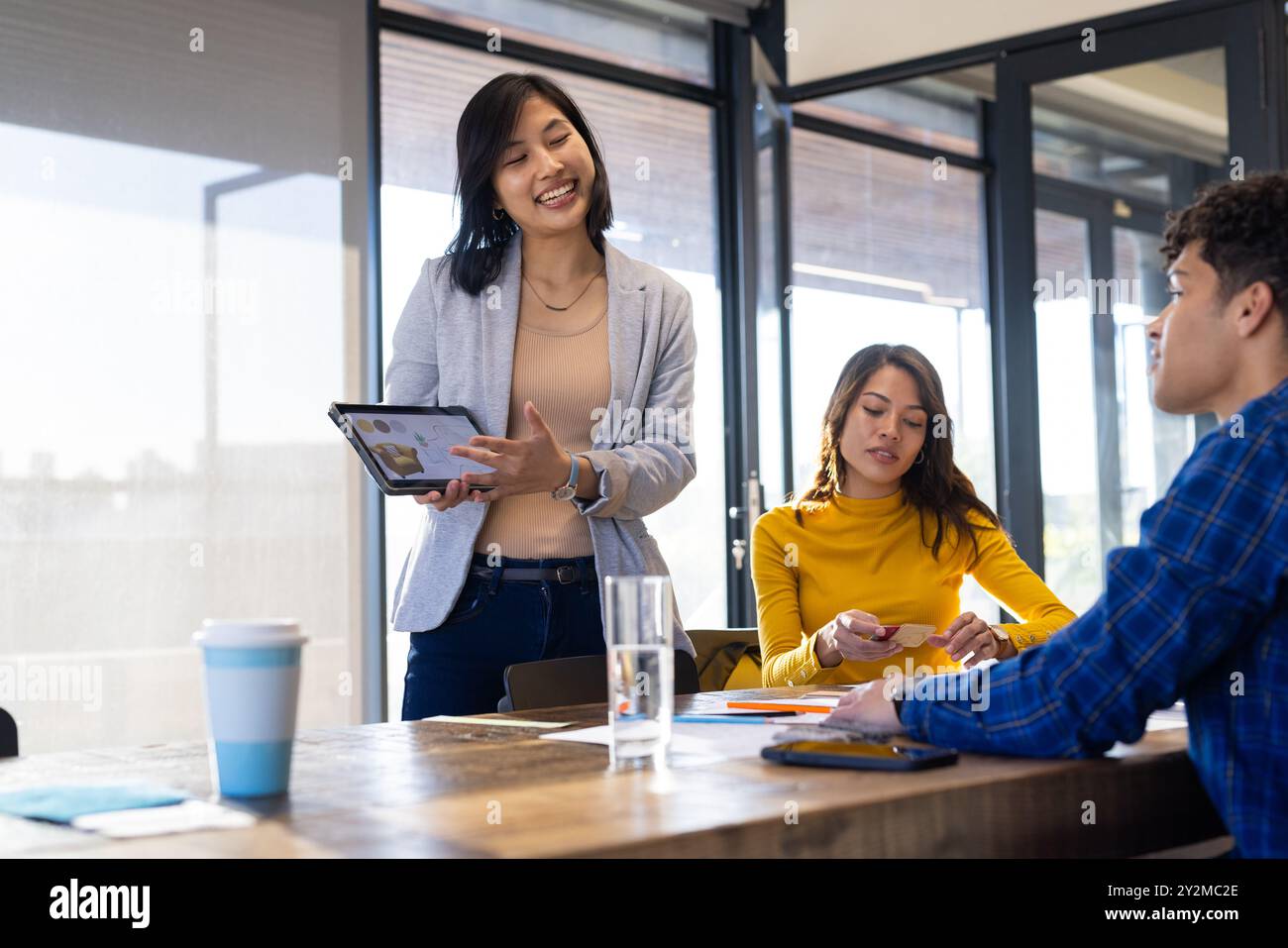 Präsentation von Designideen auf einem Tablet, asiatische Frau, die sich mit Kollegen in Besprechungen im Büro zusammensetzt Stockfoto