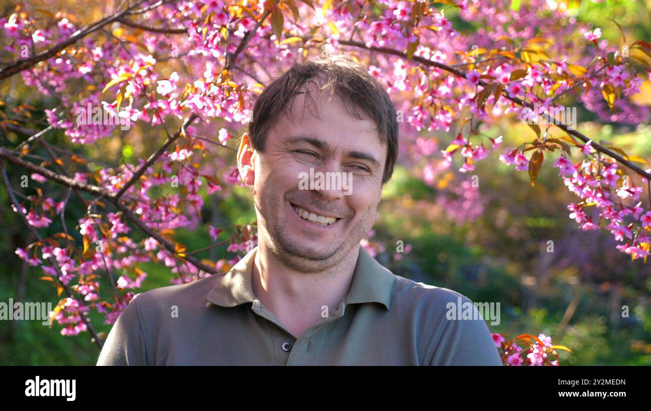 Mann lächelt und entspannt unter blühenden Kirschblüten in sonniger Sonne Stockfoto