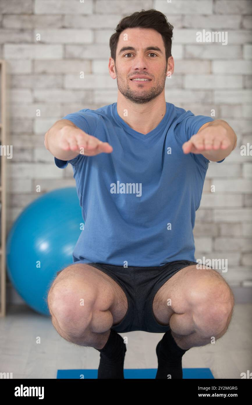 Mann, der die Balance in der Squat-Position auf der Trainingsmatte hält Stockfoto