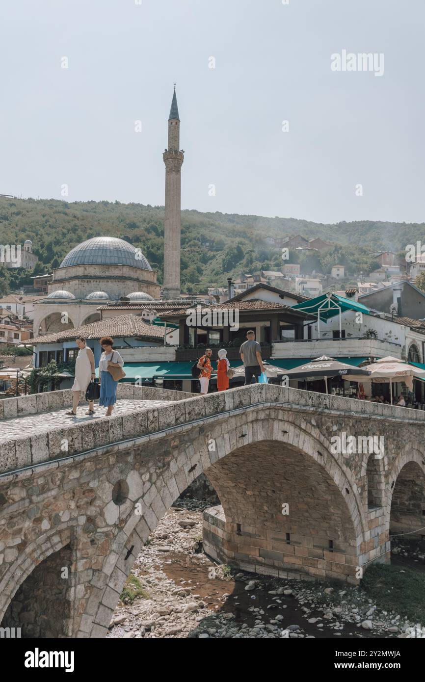 Touristen und Einheimische auf der Alten Steinbrücke über den Fluss Bistrica im Zentrum von Prizren im Kosovo, mit dem Minarett der Sinan Pascha Moschee dahinter. Stockfoto