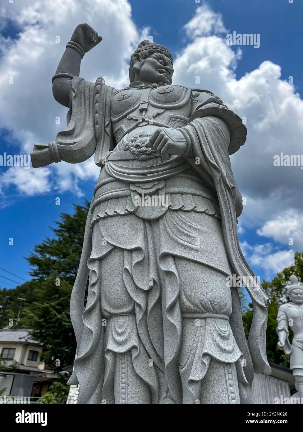 Eine Nahaufnahme einer Statue der Schutzgöttin im Ishiteji-Tempel in Matsuyama, Japan, die hoch unter einem dramatischen Himmel mit komplizierten Details auf dem Steinauto steht Stockfoto