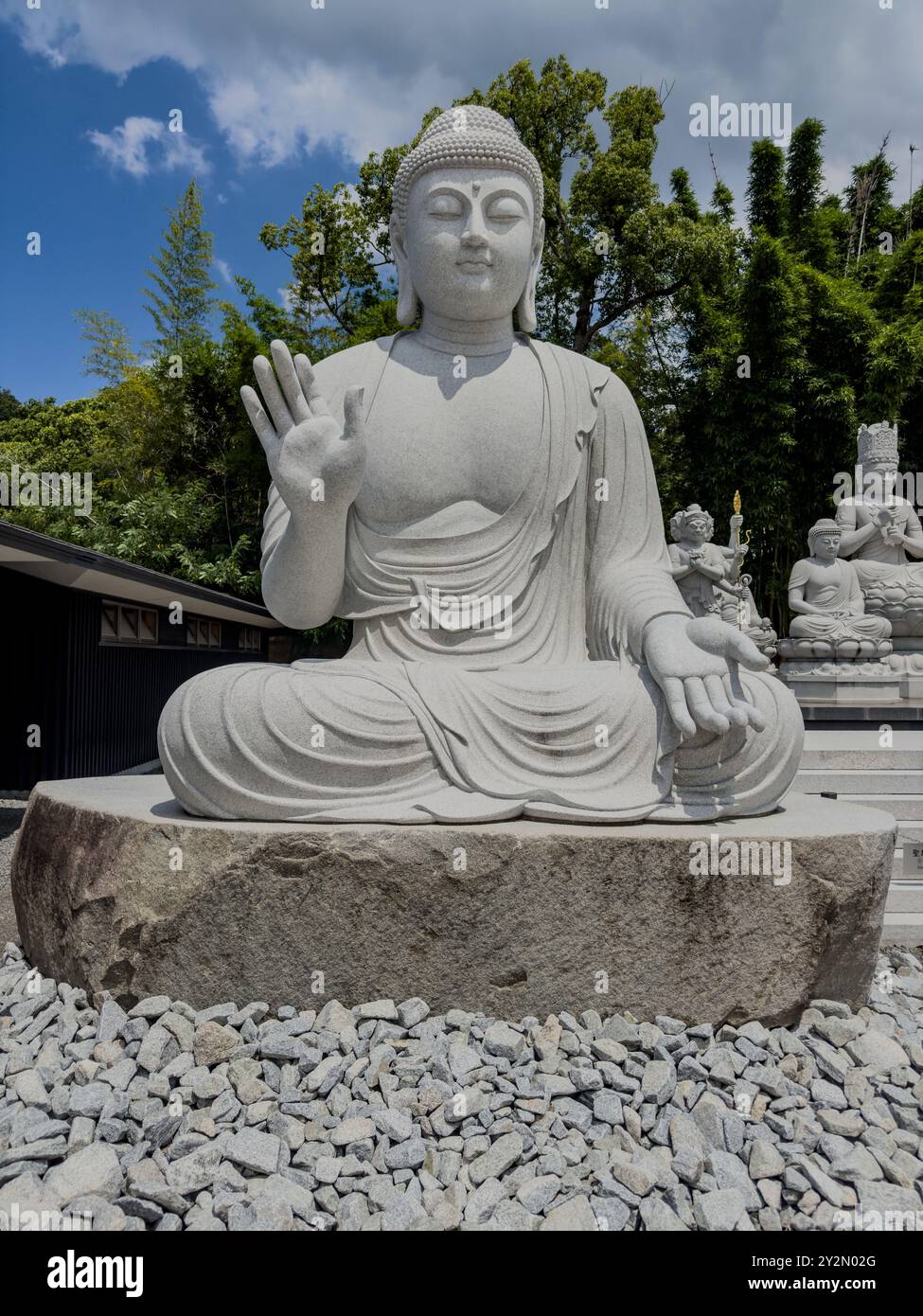 Ein Bild einer großen Buddha-Statue im Ishiteji-Tempel, Matsuyama, Japan, umgeben von kleineren Statuen und Grün in einer friedlichen Tempelanlage. Stockfoto