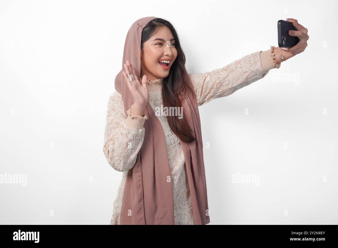 Schöne asiatische muslimische Frau im Kopftuch Hijab Schleier lachend und macht ein lustiges Selfie mit Handy, isoliert durch weißen Hintergrund Stockfoto