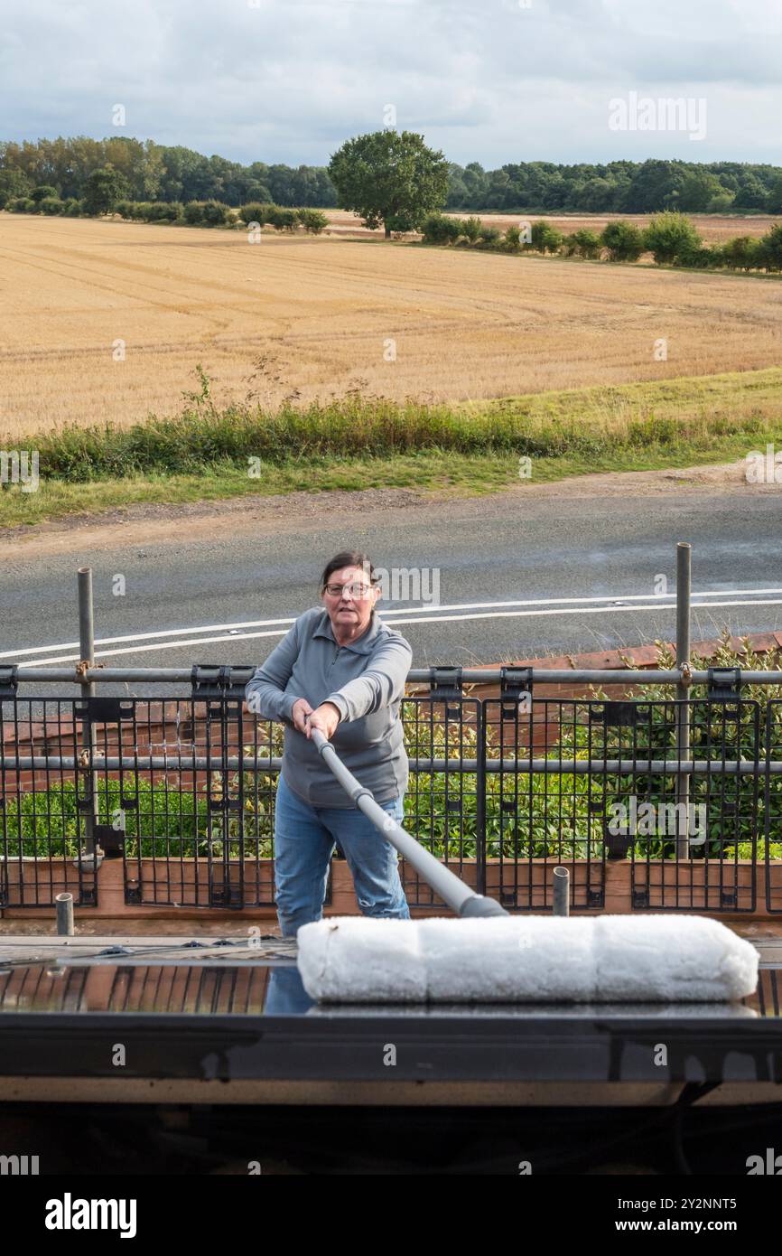 Frau, die Solarpaneele auf dem Dach eines Norfolk-Landhauses reinigt. NB: Die Räumlichkeiten auf dem Foto sind freigegebenes Eigentum. Stockfoto