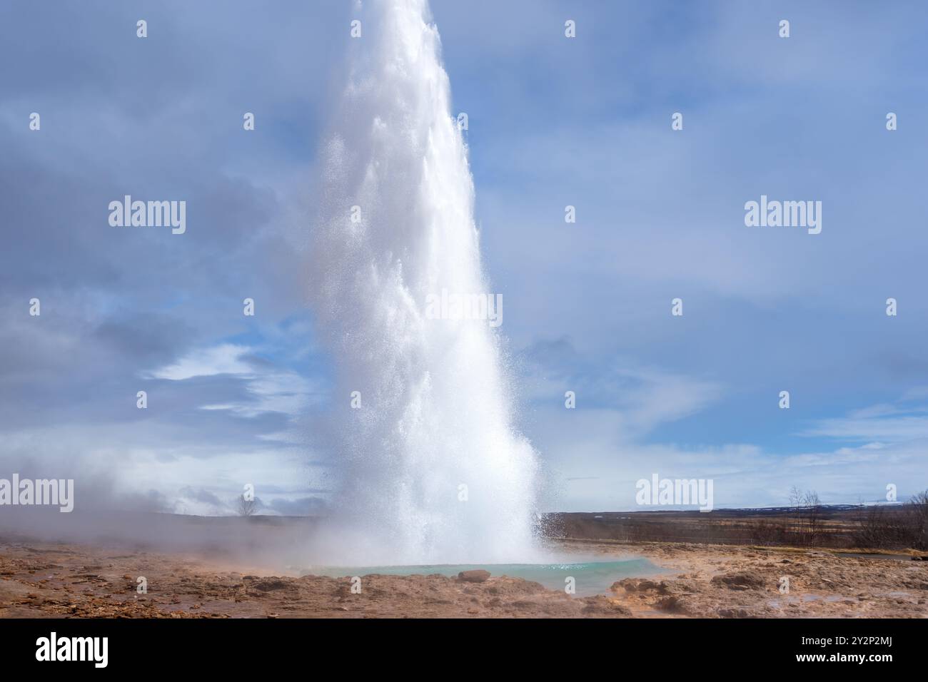 Touristen bestaunen den Strokkur Geysir, der eine Wolke Dampf und Wasser hoch in die Luft schickt. Dieses geothermische Wunder ist eine beliebte Attraktion Stockfoto