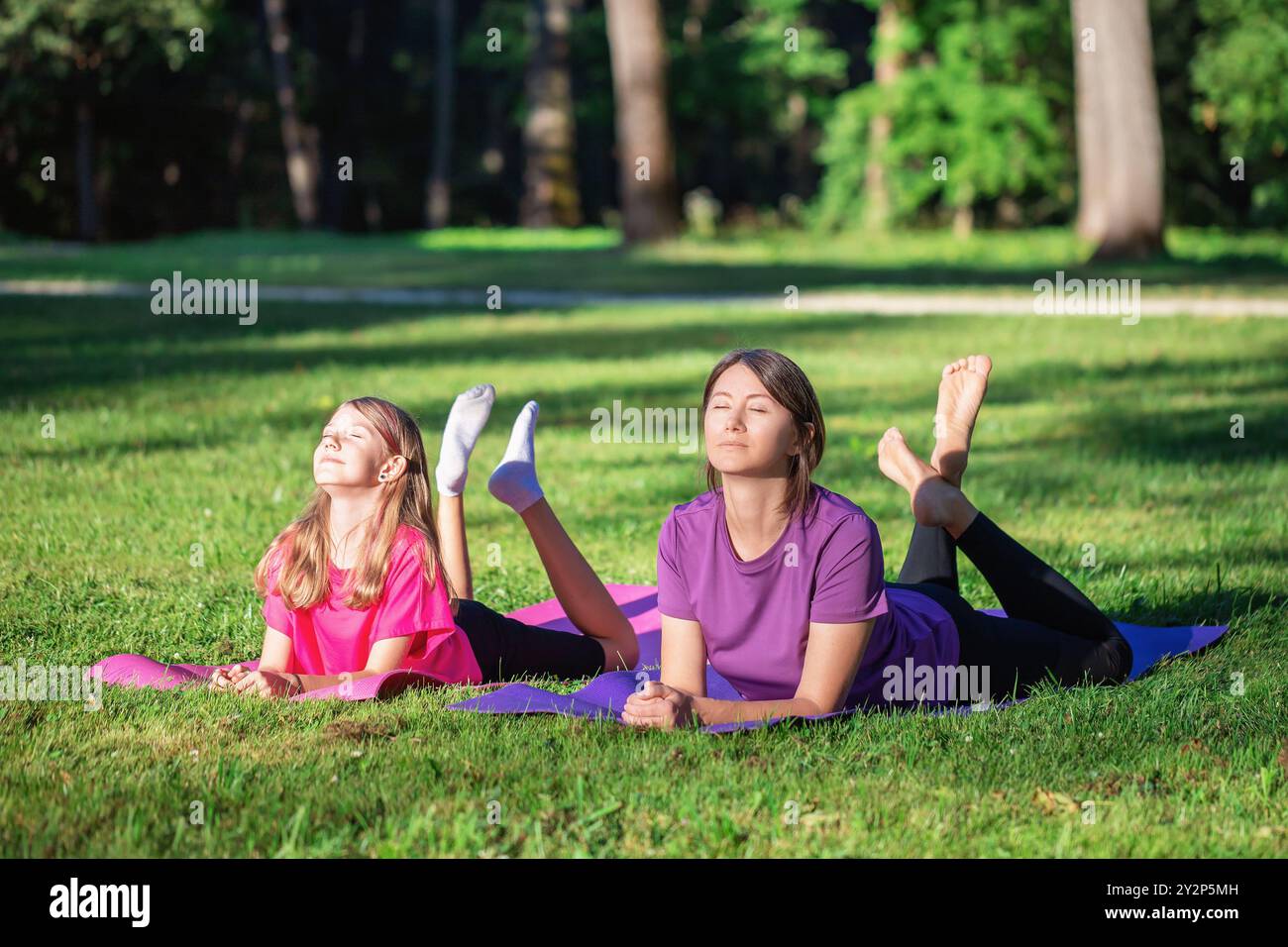 Mama und Tochter ruhen sich während des Parktrainings am sonnigen Abend auf der Matte aus, trainieren in Turnkleidung Stockfoto