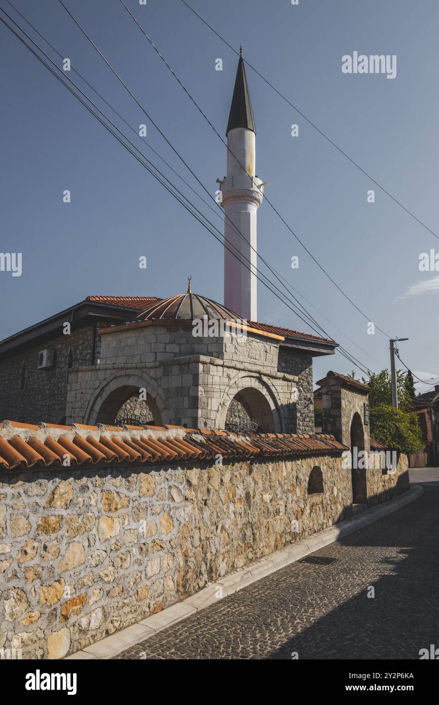 Das Äußere einer Moschee mit einem kleinen weißen Minarett, das in einen wolkenlosen blauen Himmel in der Stara Varos (Altstadt) des Stadtzentrums von Podgorica reicht. Stockfoto