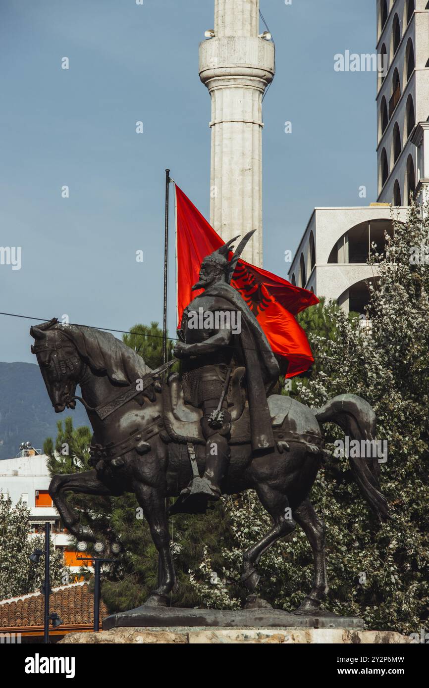 Die Statue von Skanderbeg, die auf einem Pferd reitet, mit der albanischen Flagge und dem Minarett einer Moschee im Hintergrund. Die Statue steht auf dem Skanderbeg-Platz. Stockfoto