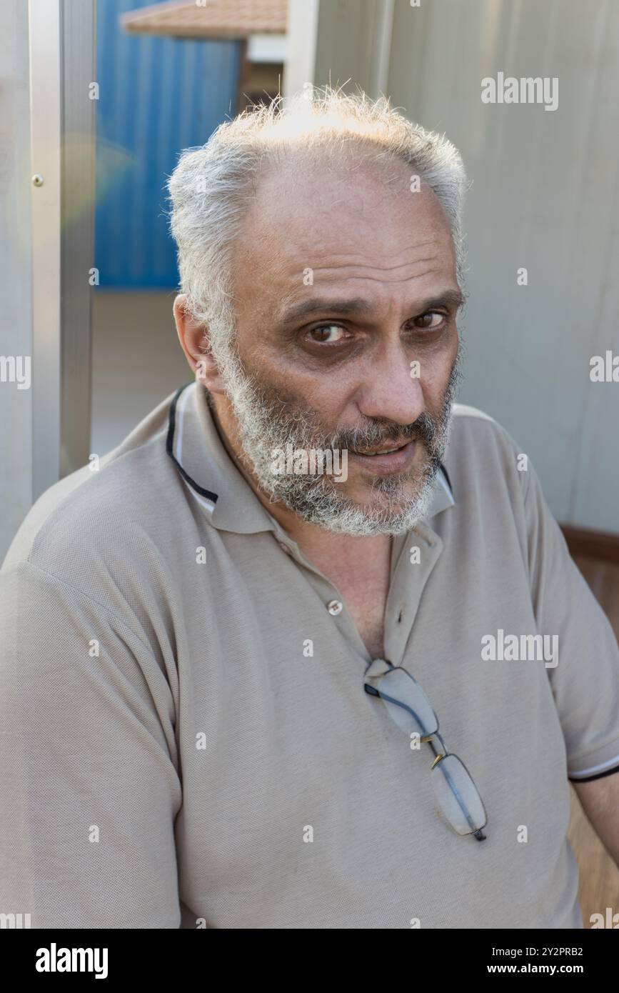 Alleinstehender alter Mann mit Bart und grauen Haaren, der draußen sitzt, halb Porträt Stockfoto