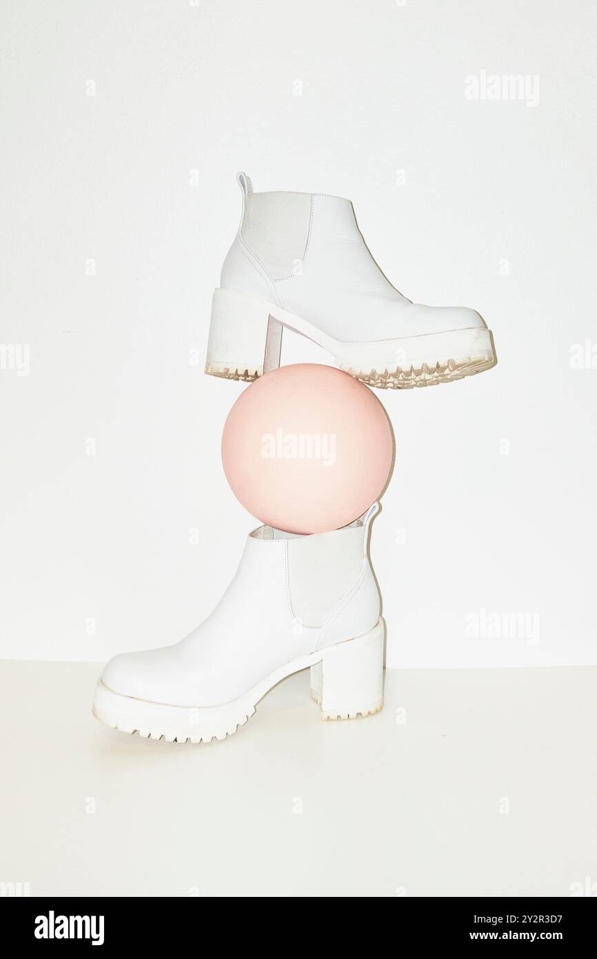 Elegante weiße Plateaustiefel in Kombination mit einer zarten rosa geometrischen Kugel schaffen ein modernes und künstlerisches Statement Stockfoto